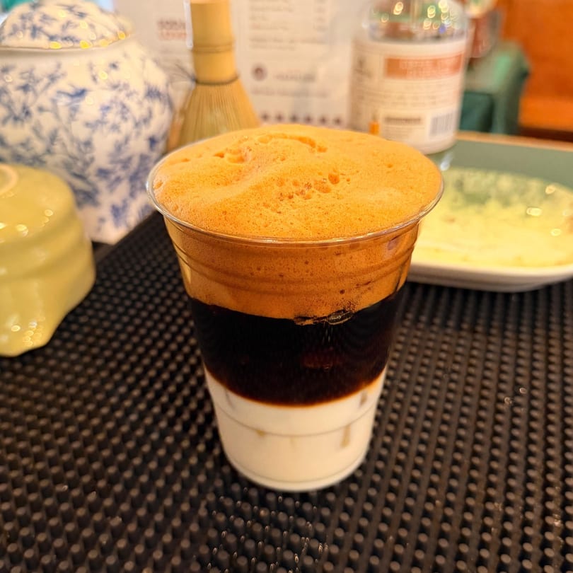 Vietnamese iced coffee with foamy top layer, dark coffee, and white condensed milk in a clear cup.