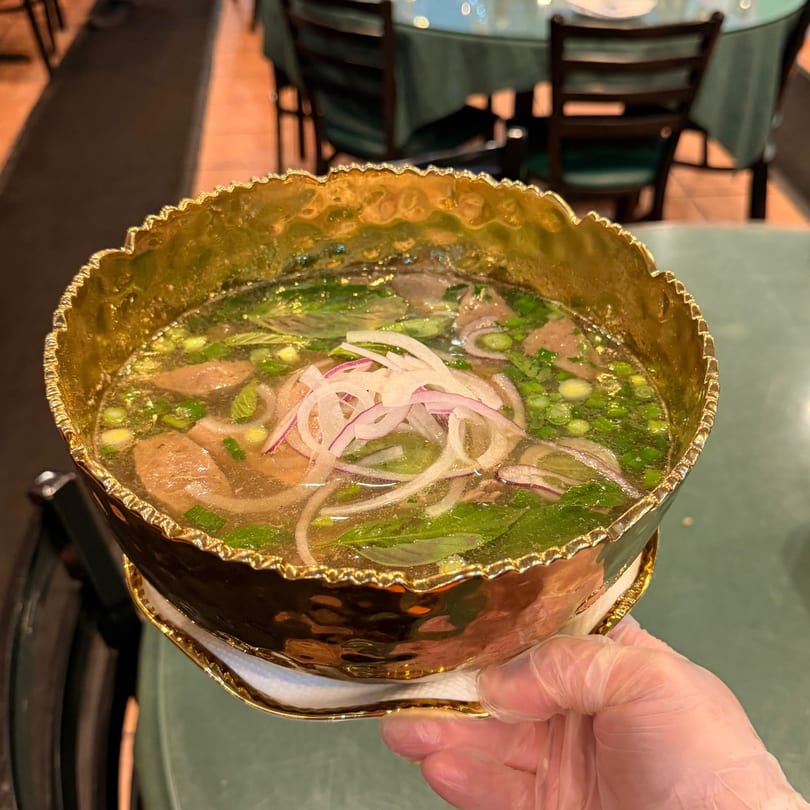 A hand in a clear glove holds a golden bowl of Pho Hoai's Vietnamese pho soup.