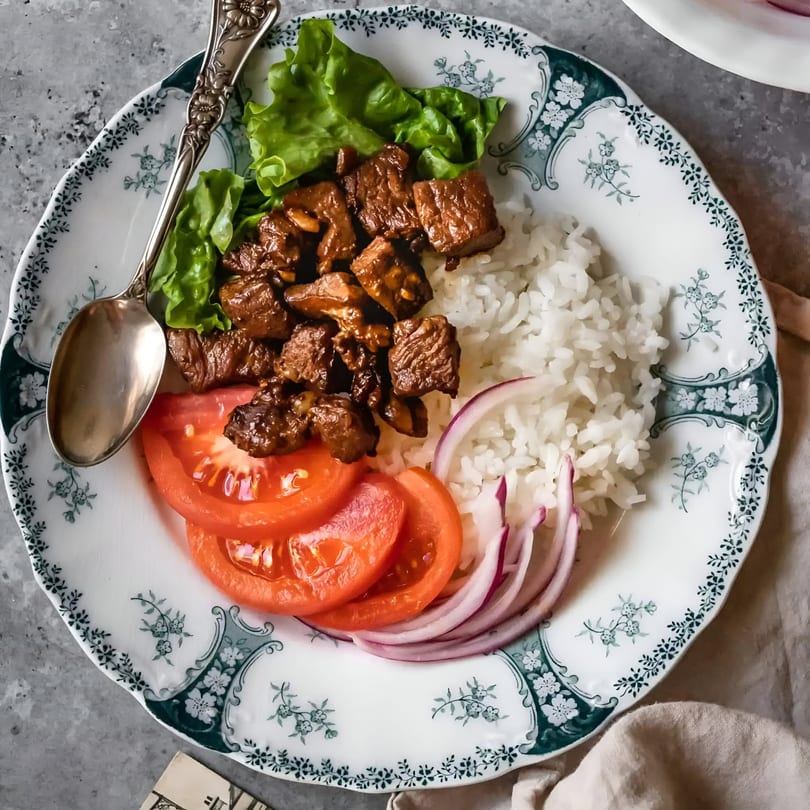 Vietnamese beef cubes with rice, lettuce, tomato, and red onion on a decorative plate.