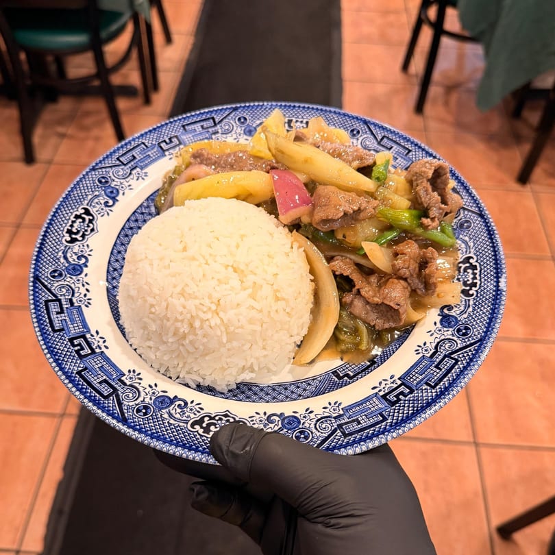 A Vietnamese beef stir-fry with potatoes, onions, and rice, served on a blue and white plate.