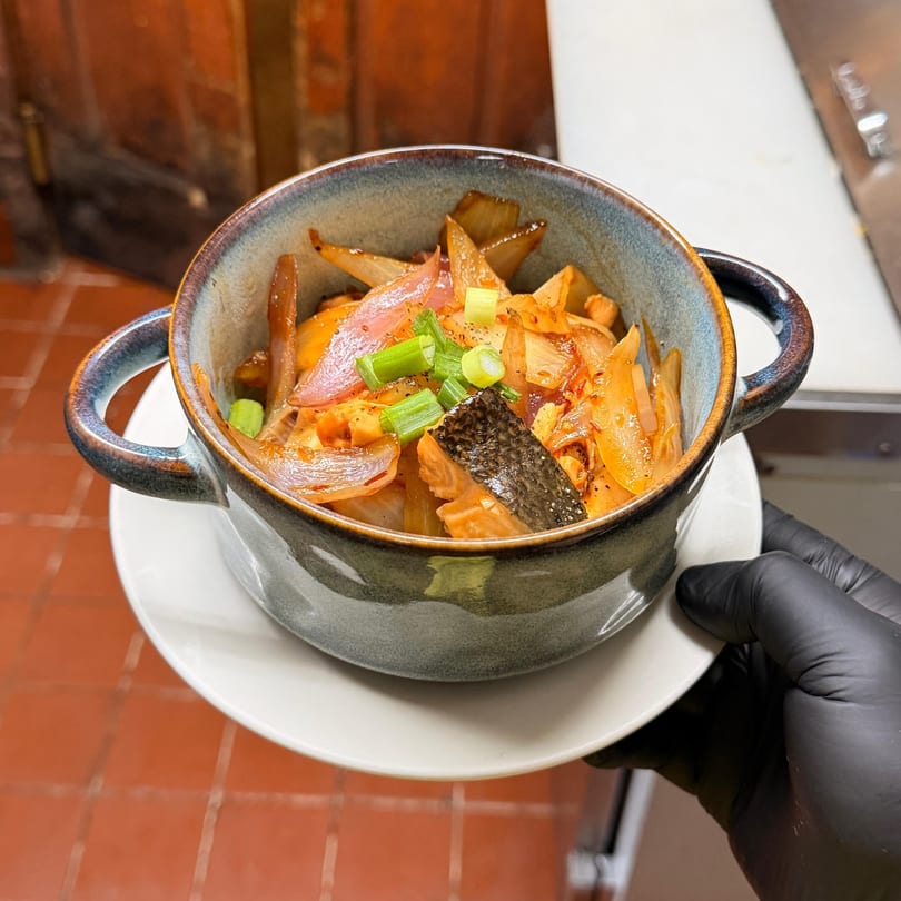 Vietnamese salmon and onions in a rustic bowl, held by a gloved hand.