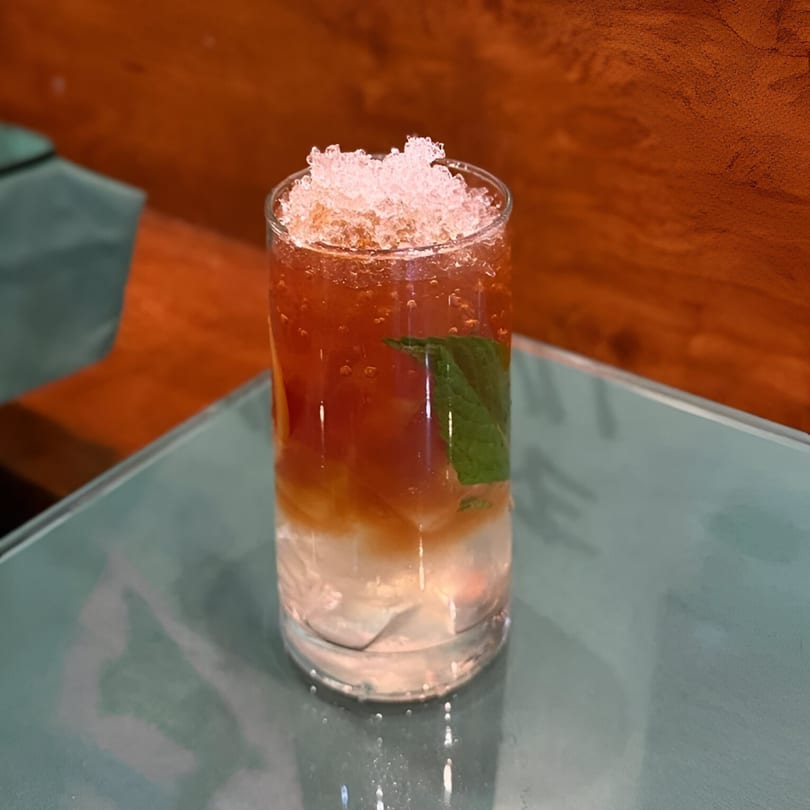 A refreshing Vietnamese iced tea with crushed ice and a mint leaf on a glass table.