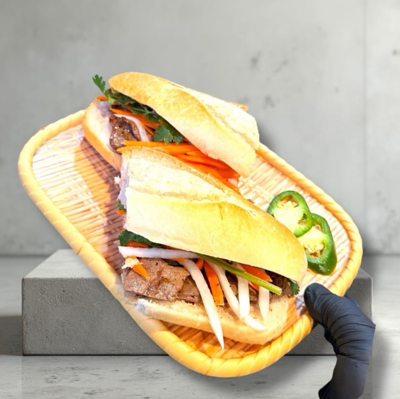 Two halves of a Vietnamese banh mi sandwich with meat and vegetables on a woven tray.