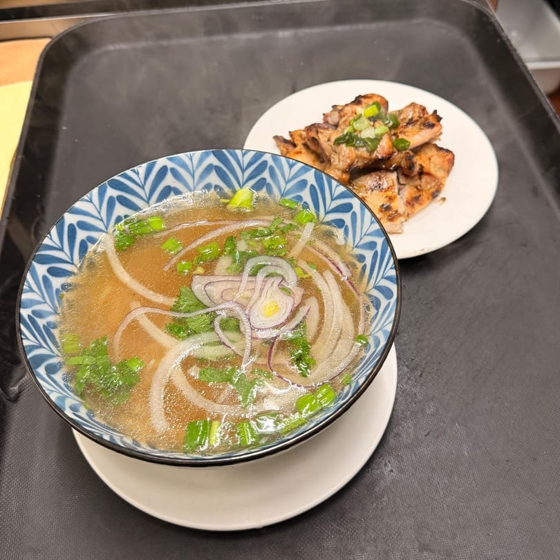 A bowl of Pho Hoai pho with onions and herbs, alongside a plate of grilled chicken.
